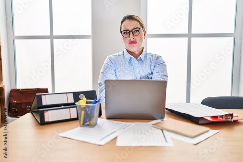 Young hispanic woman working at the office wearing glasses skeptic and nervous, disapproving expression on face with crossed arms. negative person.