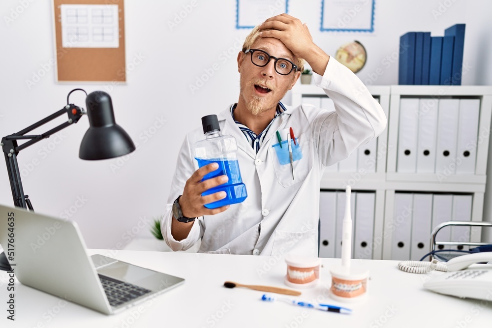 Young blond dentist man holding mouthwash at clinic stressed and frustrated with hand on head, surprised and angry face Young blond dentist man holding mouthwash at clinic stressed and frustrated with hand on head, surprised and angry face