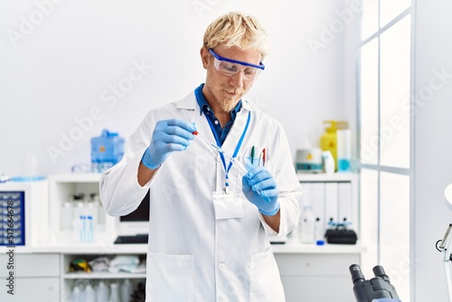 Young caucasian man wearing scientist uniform using pipette at laboratory