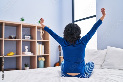 Young latin woman waking up stretching arms at bedroom