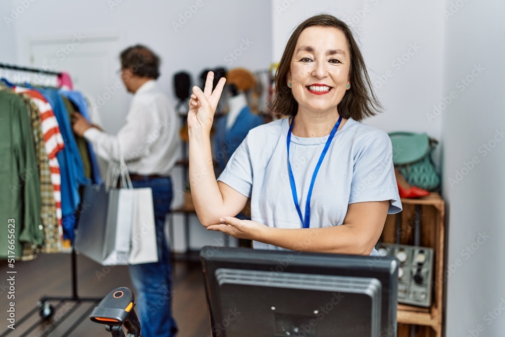 Middle age hispanic woman working as manager at retail boutique smiling with happy face winking at the camera doing victory sign. number two. Middle age hispanic woman working as manager at retail boutique smiling with happy face winking at the camera doing victory sign. number two.