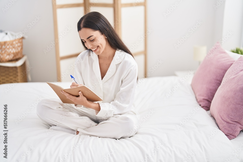 Young hispanic woman writing on notebook sitting on bed at bedroom Young hispanic woman writing on notebook sitting on bed at bedroom