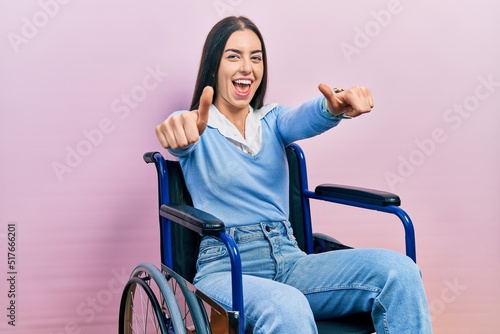 Beautiful woman with blue eyes sitting on wheelchair approving doing positive gesture with hand, thumbs up smiling and happy for success. winner gesture.