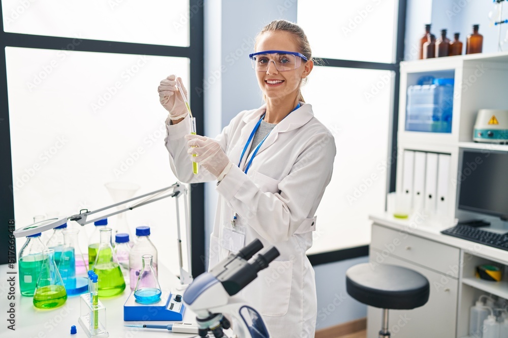 Naklejka premium Young blonde woman wearing scientist uniform working at laboratory