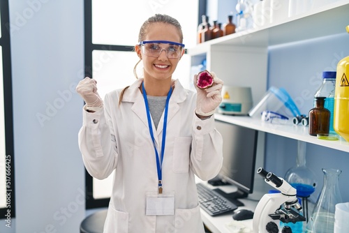 Young woman working at scientist laboratory holding geode screaming proud  celebrating victory and success very excited with raised arm