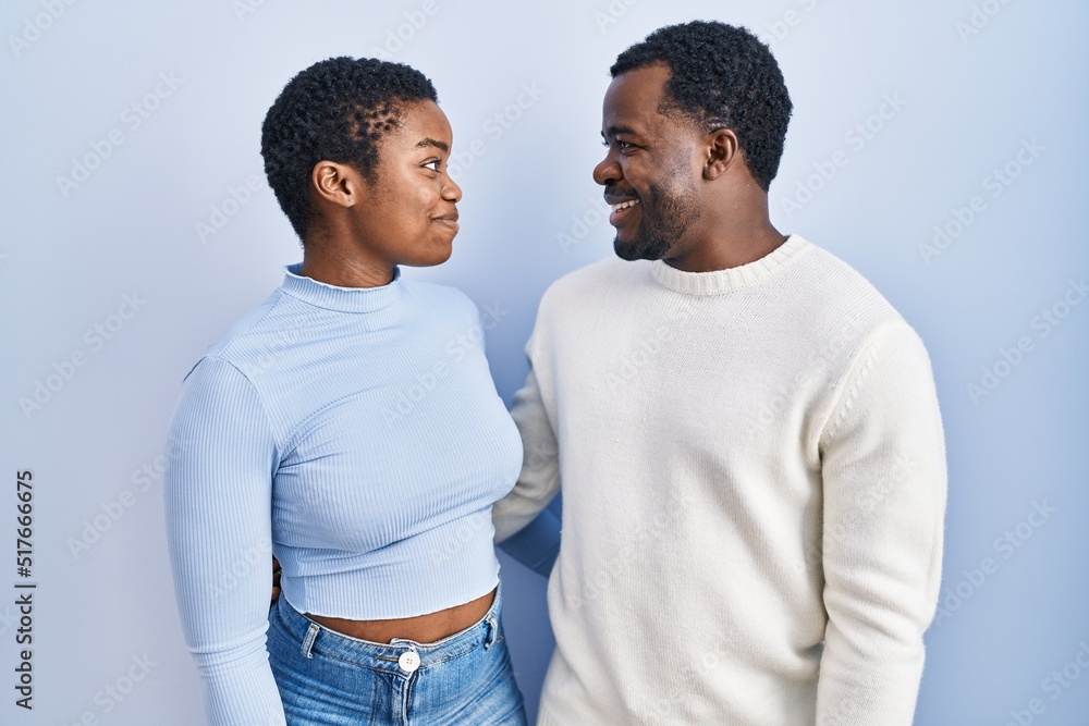 Young african american couple standing over blue background looking to side, relax profile pose with natural face and confident smile. Young african american couple standing over blue background looking to side, relax profile pose with natural face and confident smile.