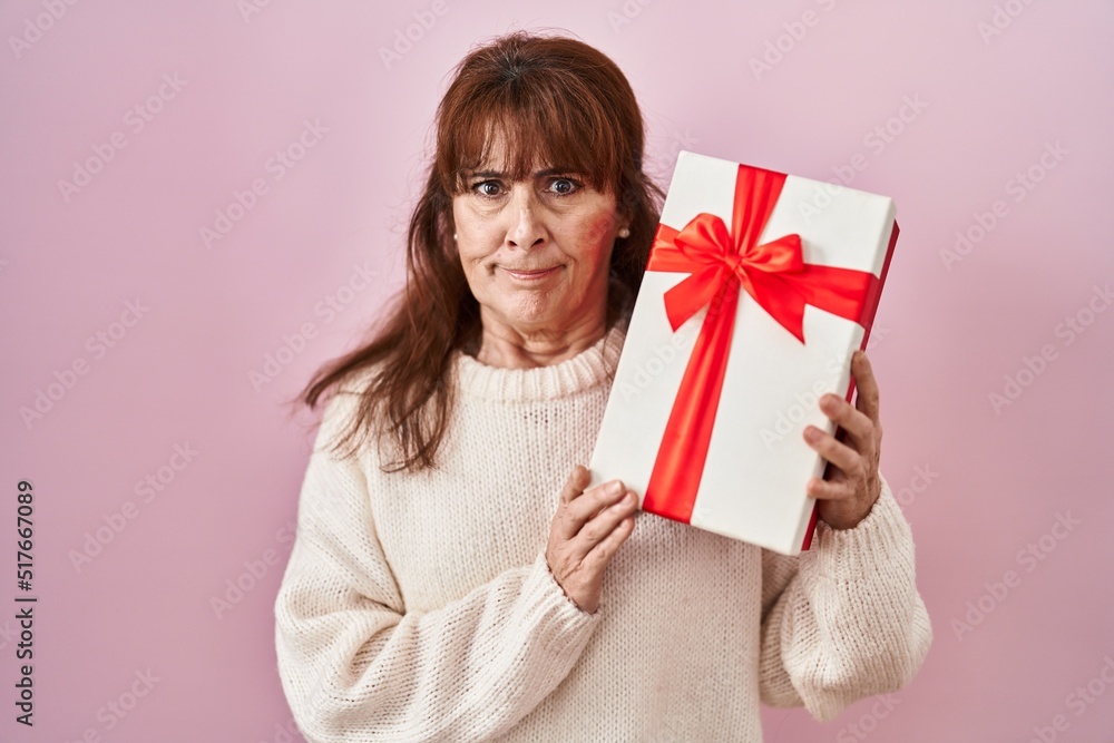 Middle age hispanic woman holding present skeptic and nervous, frowning upset because of problem. negative person. Middle age hispanic woman holding present skeptic and nervous, frowning upset because of problem. negative person.