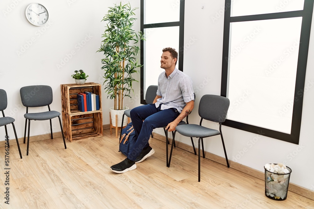 Young hispanic man smiling confident sitting on chair at waiting room