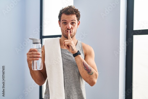 Young hispanic man wearing sportswear drinking water asking to be quiet with finger on lips. silence and secret concept. © Krakenimages.com