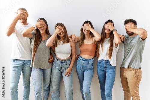 Group of young friends standing together over isolated background smiling and laughing with hand on face covering eyes for surprise. blind concept.