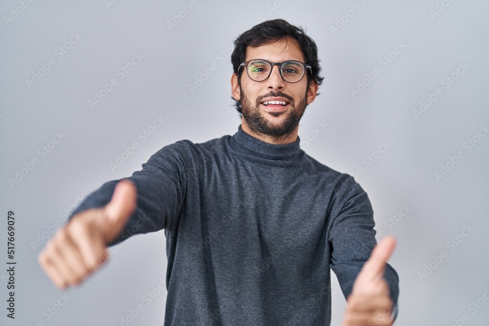 Handsome latin man standing over isolated background approving doing positive gesture with hand, thumbs up smiling and happy for success. winner gesture. Handsome latin man standing over isolated background approving doing positive gesture with hand, thumbs up smiling and happy for success. winner gesture.