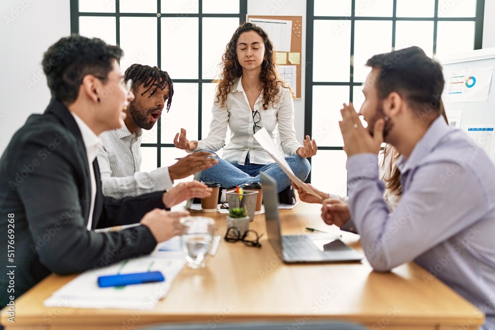 Fototapeta premium Businesswoman enjoys meditating during meeting. Sitting on desk near arguing partners at the office.