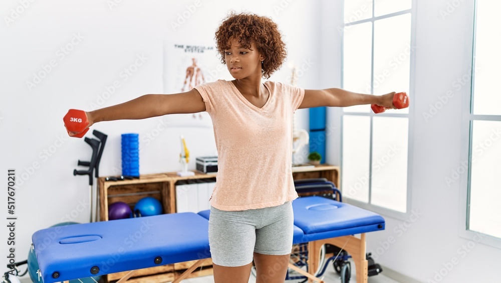 Obraz premium Young african american woman doing rehab using dumbbells at clinic
