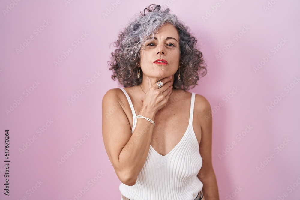 Middle age woman with grey hair standing over pink background touching painful neck, sore throat for flu, clod and infection Middle age woman with grey hair standing over pink background touching painful neck, sore throat for flu, clod and infection