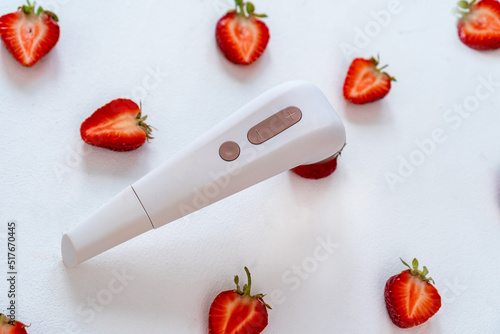 Contactless Clitoral Stimulator for adult and a strawberry cut in half imitating a female clitoris isolated on the white background. sex toys photo
