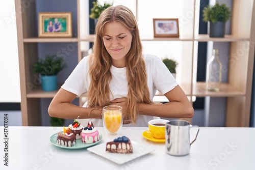 Young caucasian woman eating pastries t for breakfast with hand on stomach because indigestion, painful illness feeling unwell. ache concept. © Krakenimages.com