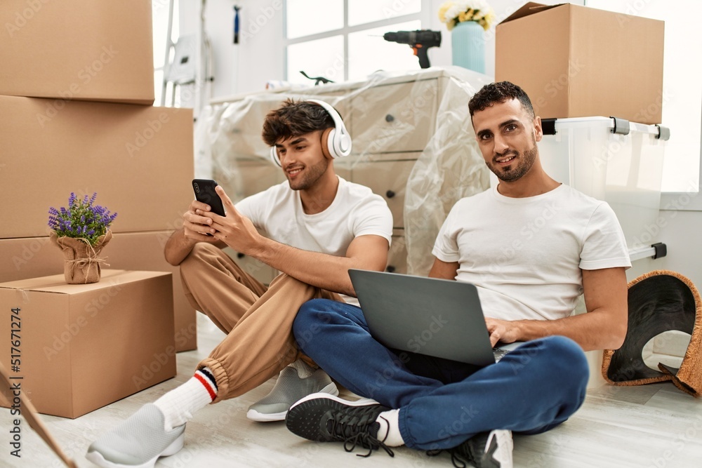 Two hispanic men couple using laptop and smartphone at new home