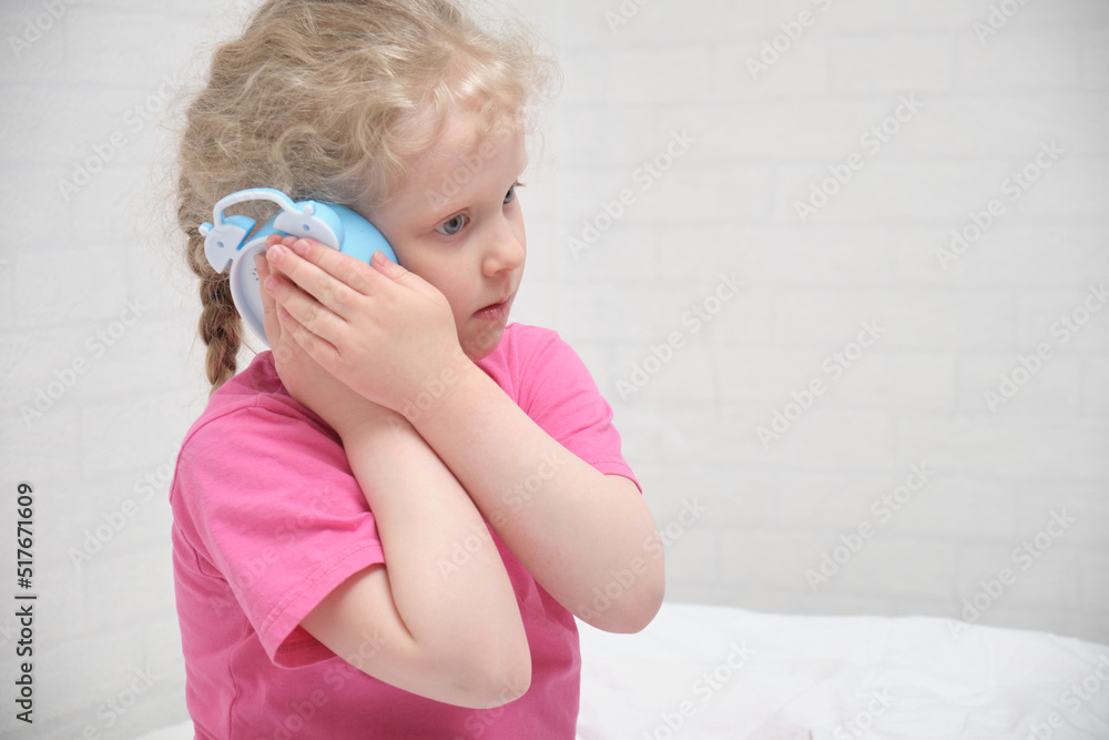 preschooler girl in a pink t-shirt hears the ticking of an alarm clock, children's healthy sleep concept preschooler girl in a pink t-shirt hears the ticking of an alarm clock, children's healthy sleep concept
