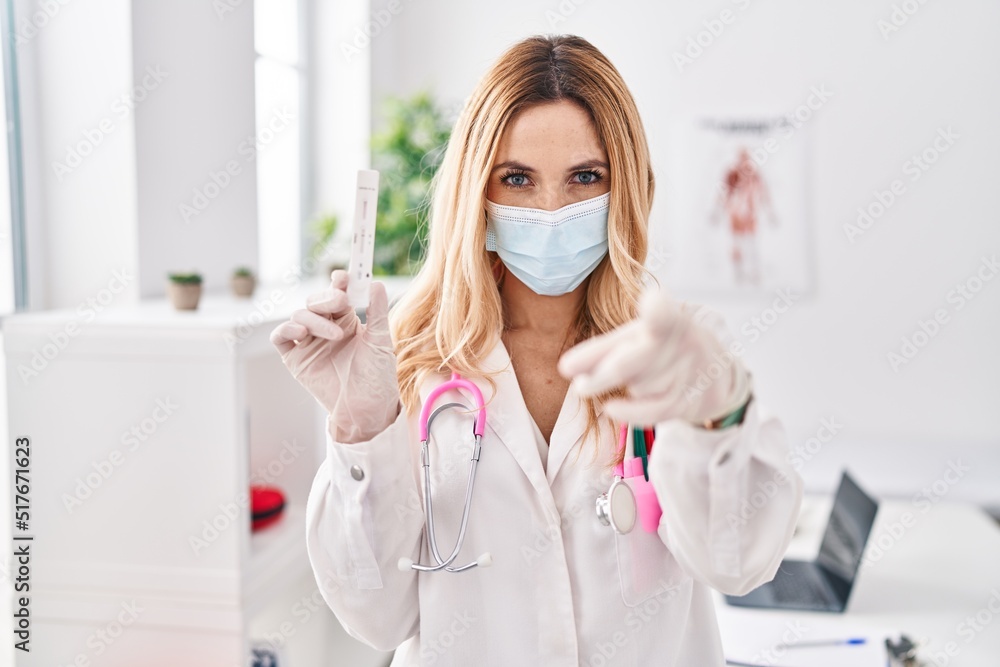 Young caucasian doctor woman holding covid test pointing with finger to the camera and to you, confident gesture looking serious Young caucasian doctor woman holding covid test pointing with finger to the camera and to you, confident gesture looking serious