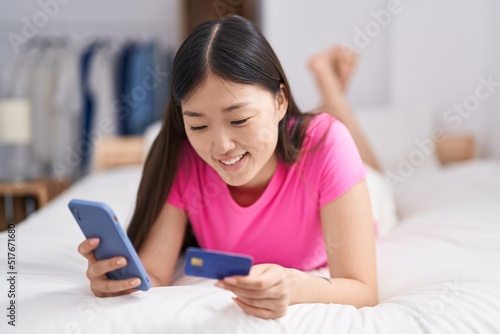 Chinese woman using smartphone and credit card lying on bed at bedroom