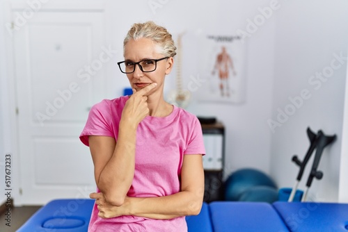 Middle age blonde woman at pain recovery clinic looking confident at the camera with smile with crossed arms and hand raised on chin. thinking positive.