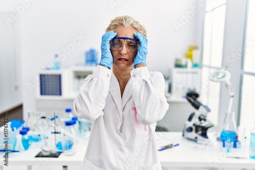 Middle age blonde woman working at scientist laboratory with hand on head for pain in head because stress. suffering migraine.