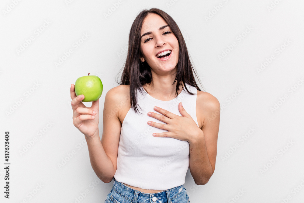 Young caucasian woman holding an apple isolated on white background laughs out loudly keeping hand on chest. Young caucasian woman holding an apple isolated on white background laughs out loudly keeping hand on chest.