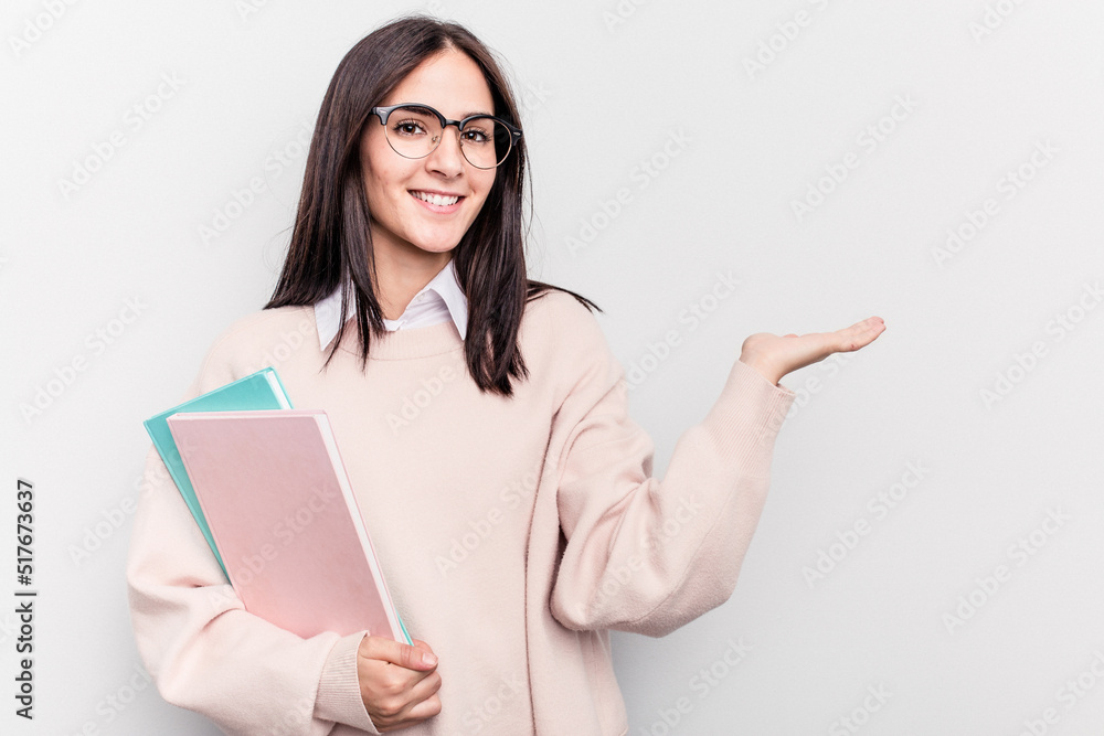 Young student caucasian woman isolated on white background showing a copy space on a palm and holding another hand on waist. Young student caucasian woman isolated on white background showing a copy space on a palm and holding another hand on waist.
