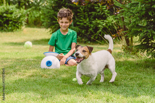 Happy boy and dog playing with automatic throw and fetch machine launching tennis balls