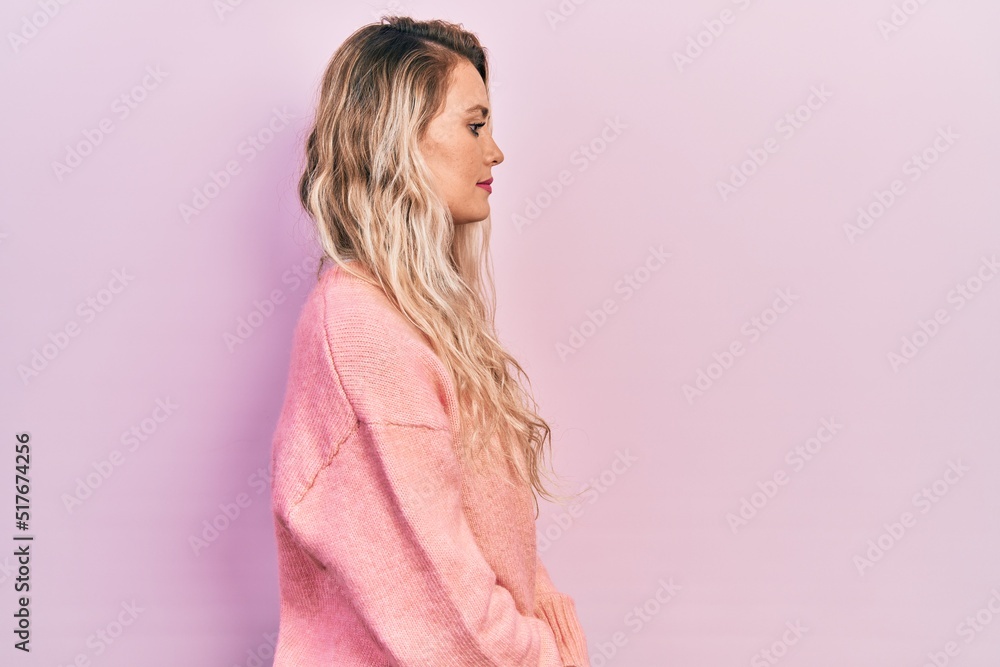 Beautiful young blonde woman wearing pink sweater looking to side, relax profile pose with natural face with confident smile. Beautiful young blonde woman wearing pink sweater looking to side, relax profile pose with natural face with confident smile.