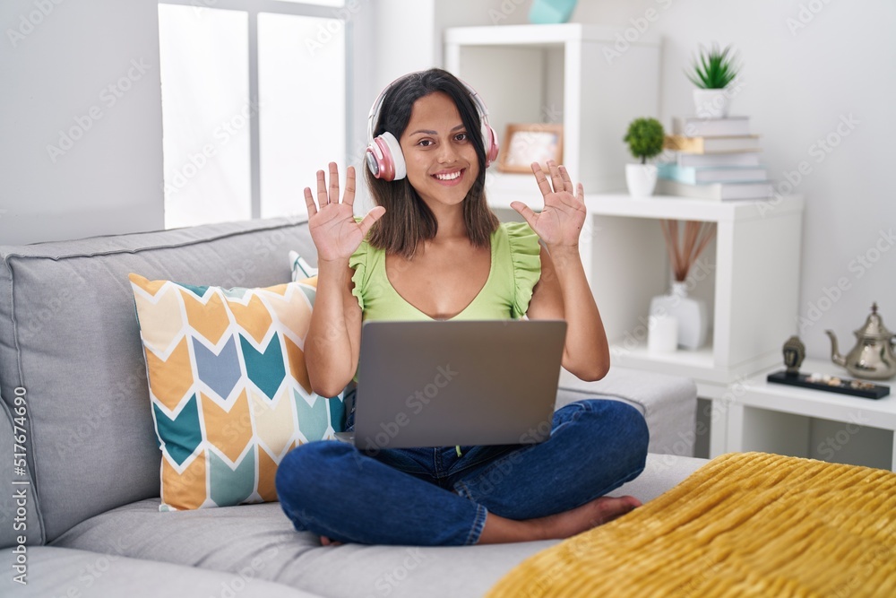 Hispanic young woman using laptop at home showing and pointing up with fingers number ten while smiling confident and happy. Hispanic young woman using laptop at home showing and pointing up with fingers number ten while smiling confident and happy.