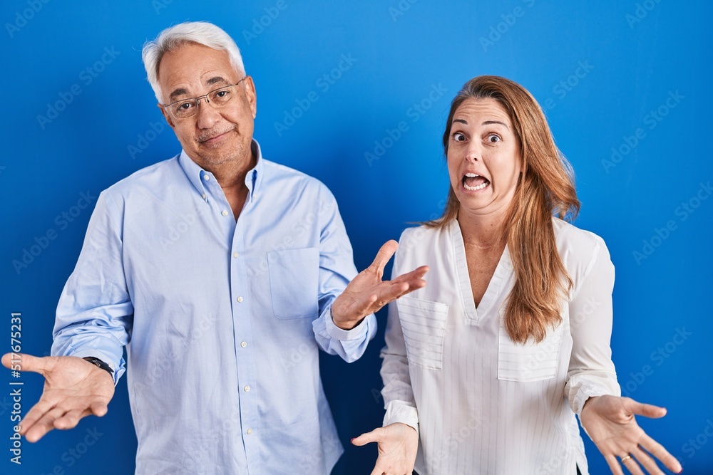 Middle age hispanic couple standing over blue background smiling cheerful with open arms as friendly welcome, positive and confident greetings Middle age hispanic couple standing over blue background smiling cheerful with open arms as friendly welcome, positive and confident greetings