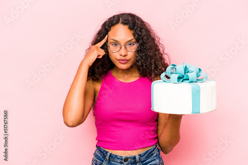 Young caucasian woman holding a cake isolated on pink background pointing temple with finger, thinking, focused on a task.