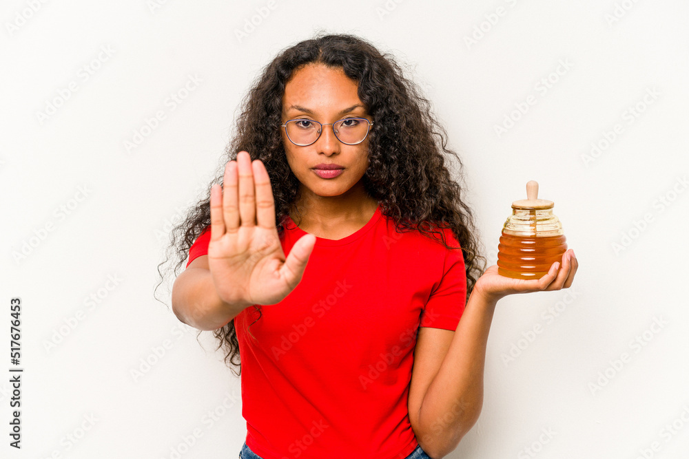 Young hispanic woman holding honey jar isolated on white background standing with outstretched hand showing stop sign, preventing you. Young hispanic woman holding honey jar isolated on white background standing with outstretched hand showing stop sign, preventing you.