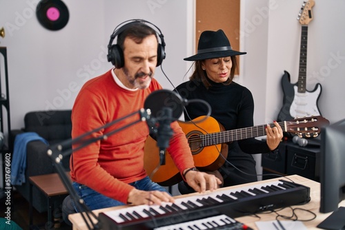 Middle age man and woman musicians playing guitar and keyboard piano singing song at music studio