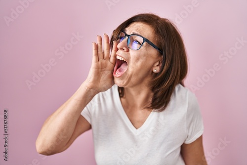 Middle age hispanic woman standing over pink background shouting and screaming loud to side with hand on mouth. communication concept.