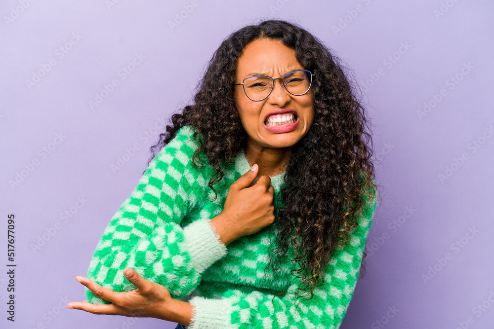 Young hispanic woman isolated on purple background massaging elbow, suffering after a bad movement. Young hispanic woman isolated on purple background massaging elbow, suffering after a bad movement.