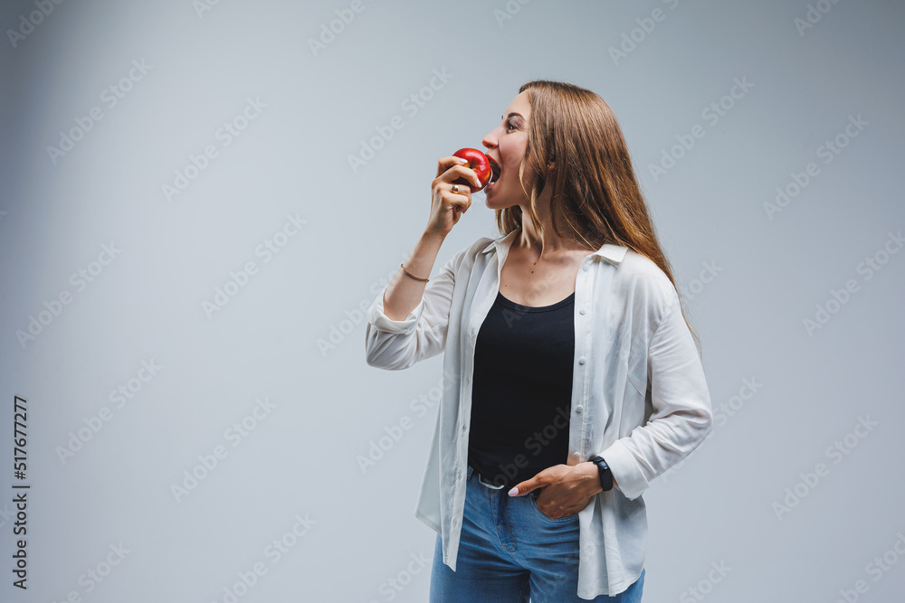 Cute brunette woman in white shirt holding red apple in hand standing on isolated white background dietetics and nutrition. Healthy food Cute brunette woman in white shirt holding red apple in hand standing on isolated white background dietetics and nutrition. Healthy food