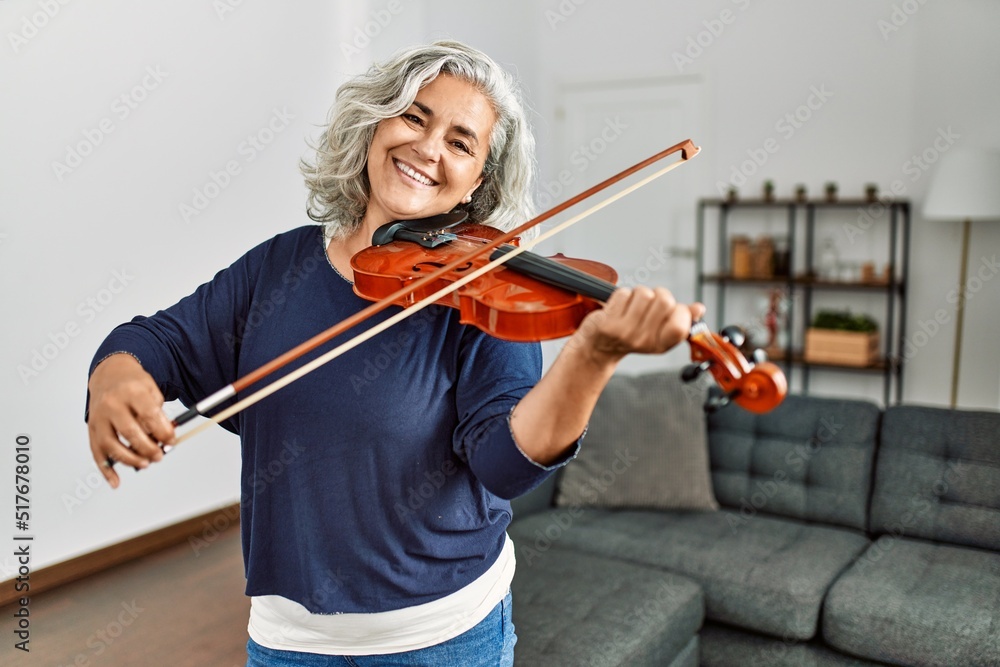 Middle age grey-haired artist woman playing violin standing at home. Middle age grey-haired artist woman playing violin standing at home.