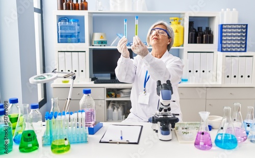 Middle age woman wearing scientist uniform looking test tubes at laboratory