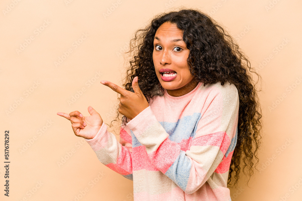 Young hispanic woman isolated on beige background pointing with forefingers to a copy space, expressing excitement and desire. Young hispanic woman isolated on beige background pointing with forefingers to a copy space, expressing excitement and desire.