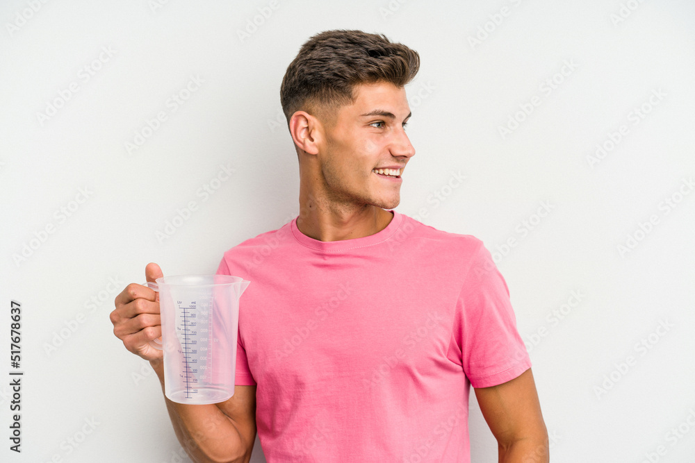 Young caucasian man holding measuring jug isolated on white background looks aside smiling, cheerful and pleasant. Young caucasian man holding measuring jug isolated on white background looks aside smiling, cheerful and pleasant.