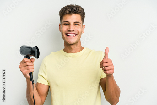 Young caucasian man holding hairdryer isolated on white background smiling and raising thumb up