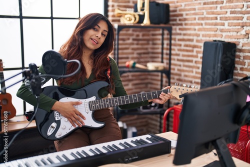 Young hispanic woman artist playing electrical guitar at music studio