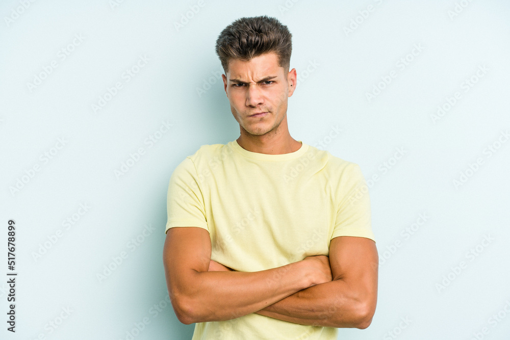 Young caucasian man isolated on blue background frowning face in displeasure, keeps arms folded. Young caucasian man isolated on blue background frowning face in displeasure, keeps arms folded.