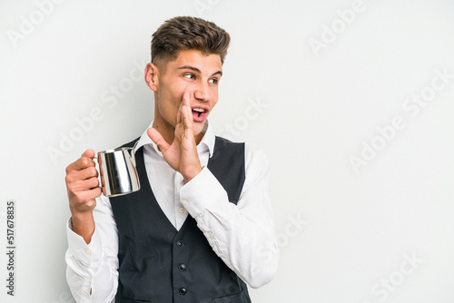 Young caucasian barista man isolated on yellow background is saying a secret hot braking news and looking aside © Asier