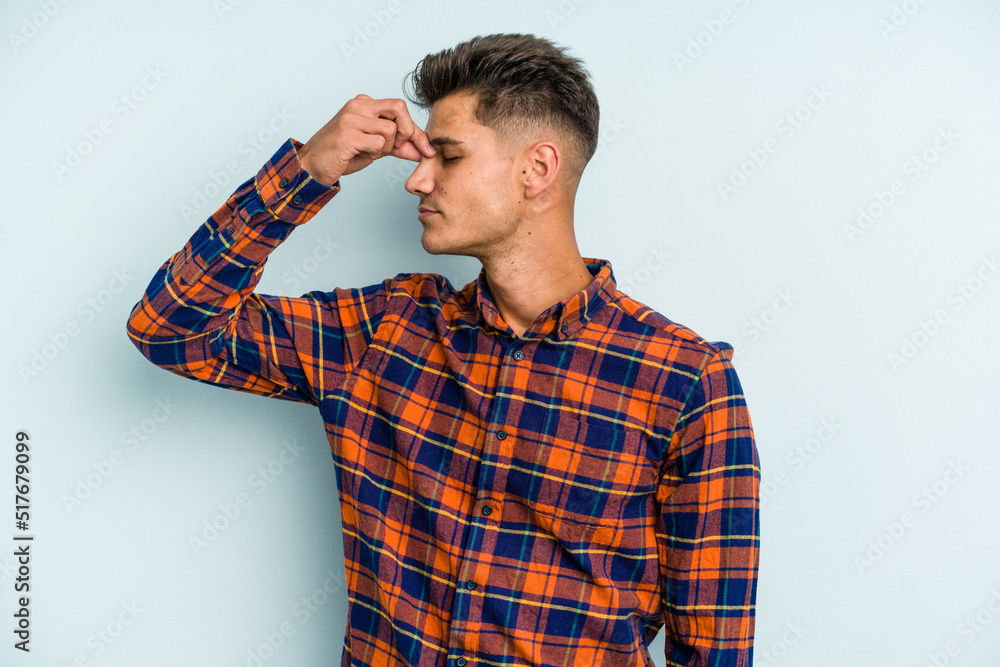 Young caucasian man isolated on blue background having a head ache, touching front of the face. Young caucasian man isolated on blue background having a head ache, touching front of the face.