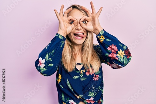 Fotografie, Obraz Young caucasian woman wearing casual clothes doing ok gesture like binoculars sticking tongue out, eyes looking through fingers