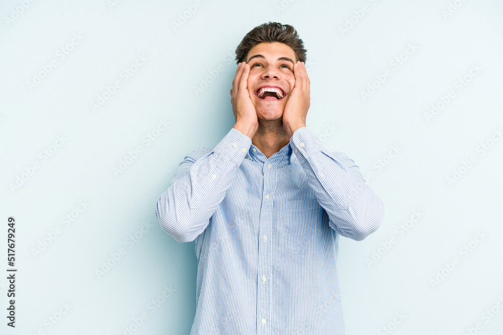 Young caucasian man isolated on blue background laughs joyfully keeping hands on head. Happiness concept. Young caucasian man isolated on blue background laughs joyfully keeping hands on head. Happiness concept.