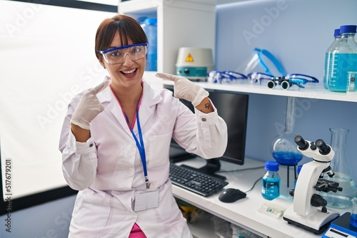 Young brunette woman working at scientist laboratory smiling cheerful showing and pointing with fingers teeth and mouth. dental health concept.